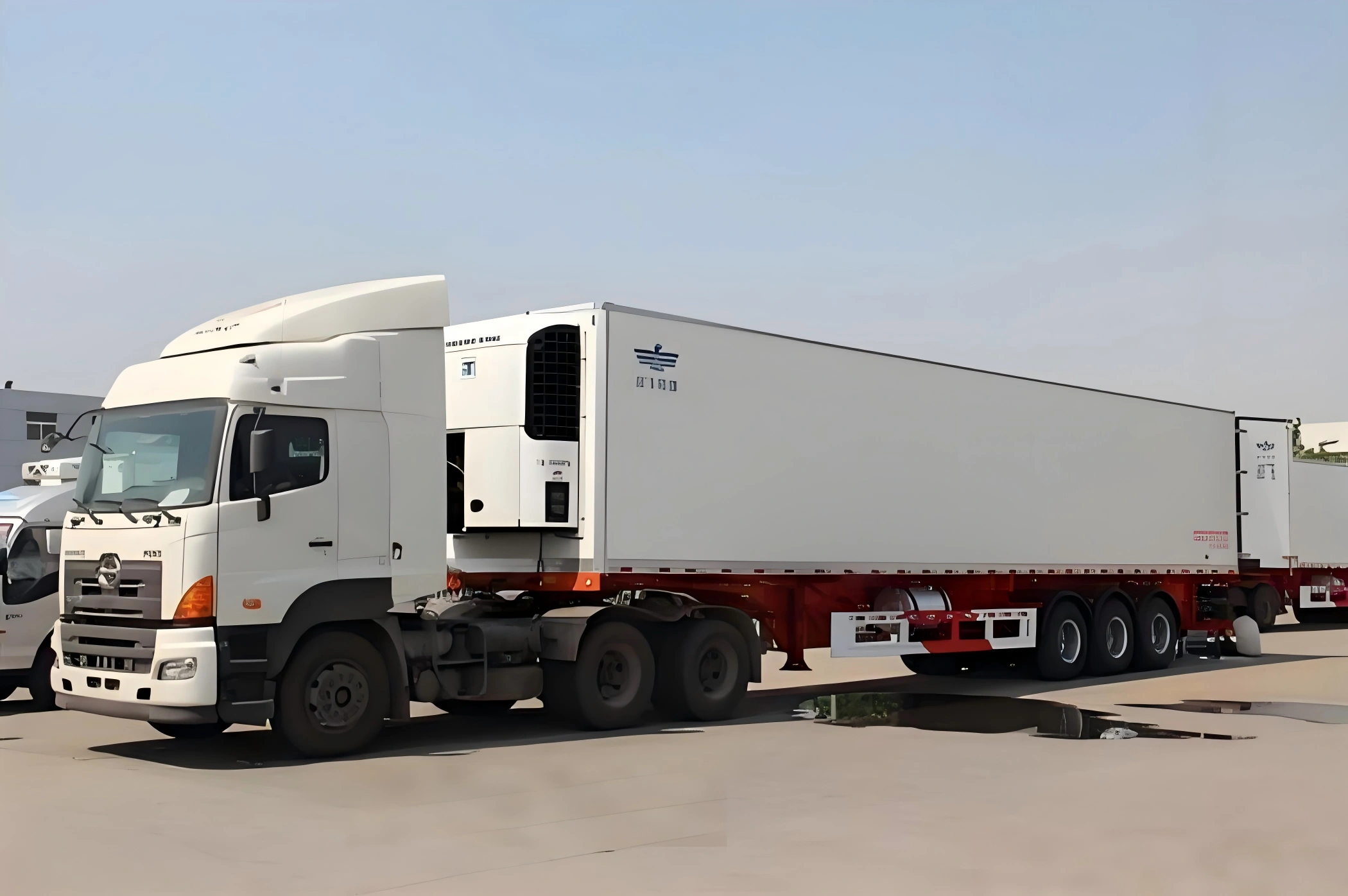 HINO prime mover connected to white refrigerated trailer with red chassis ready for road-based cold chain transportation of perishable goods