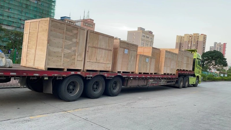 A long flatbed truck transporting multiple large, fumigation-free wooden export crates through an urban area, demonstrating secure lashing and logistics for heavy equipment overland.