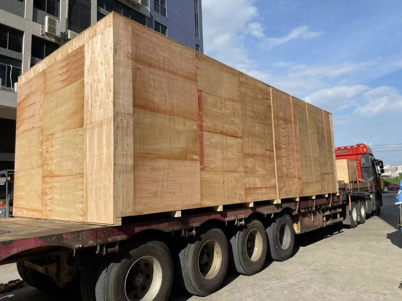 A large industrial machine is fully encased in protective foil wrapping and secured with orange strapping on a wooden pallet, ready for safe storage and transportation in a warehouse environment.