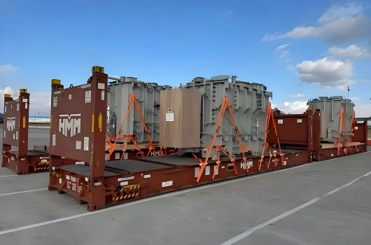 Three heavy power transformers mounted on HMM flat racks and secured with orange A frame braces and tension straps for safe transport