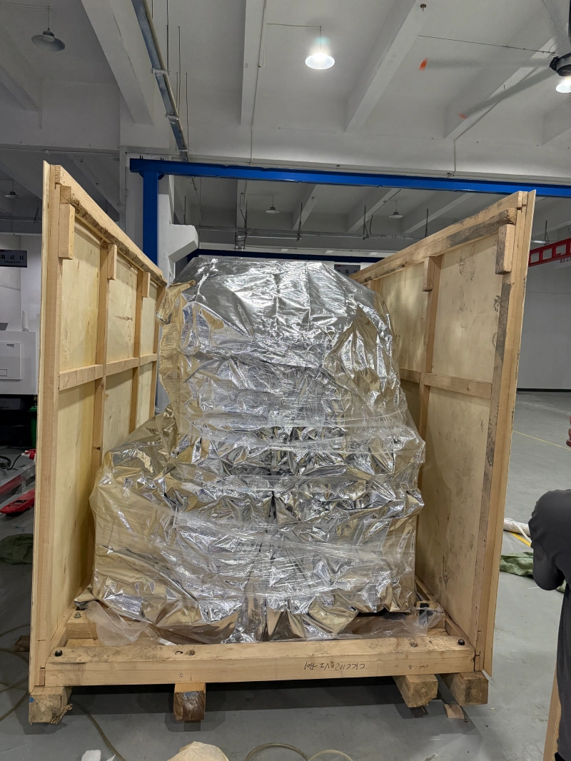 An industrial machine, fully wrapped in a vacuum-sealed aluminum foil bag for moisture and corrosion protection, is positioned inside a sturdy wooden export crate ready for final sealing.