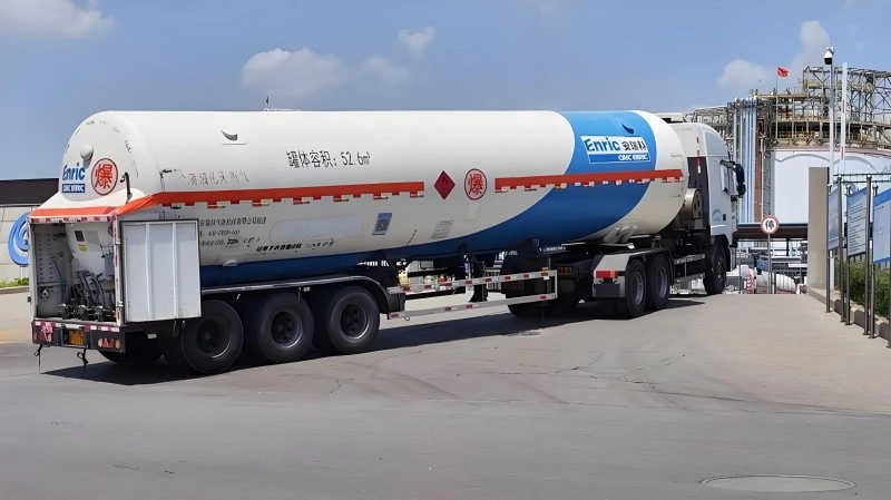 A white and blue LNG tanker truck equipped with IoT sensors, transporting oversized liquefied natural gas cargo safely through industrial areas.
