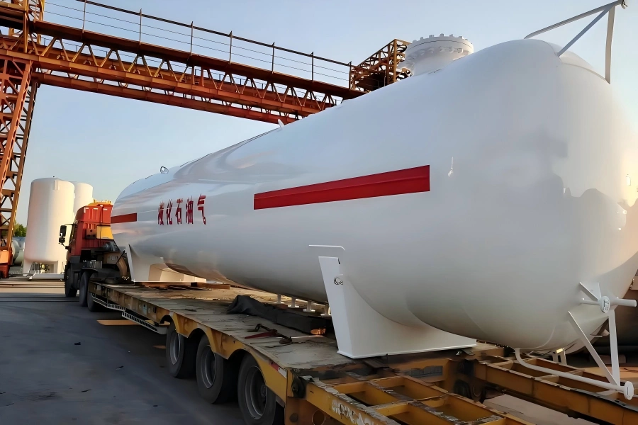 White liquefied petroleum gas tank with red hazard band and English labeling Liquefied Petroleum Gas mounted on yellow ultra low bed trailer for safe transport to oil and gas site