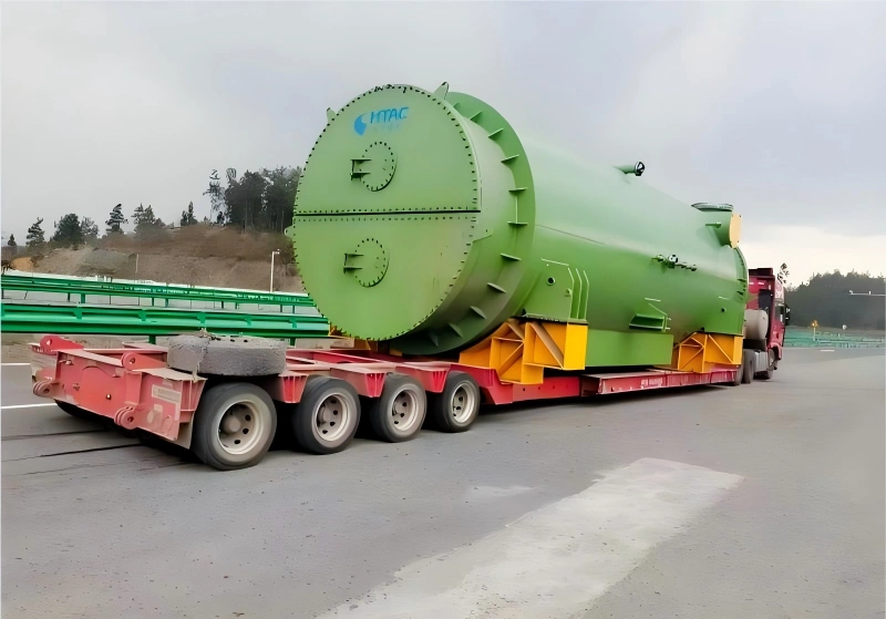 Hitachi industrial pressure vessel transported on a red multi axle lowbed trailer during inland oversized cargo movement