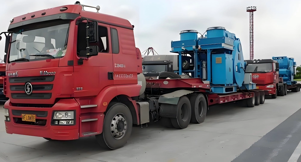 Red Sinotruk M3000 tractor unit hauling blue oversized industrial machine on extended lowbed trailer in multi truck convoy for factory delivery