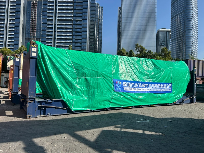 A large shipment on a blue flat rack container is covered with a reinforced green tarpaulin and lashing belts, with a banner for "Shenzhen Bentlee Supply Chain Management," demonstrating protection against environmental risks during port storage.