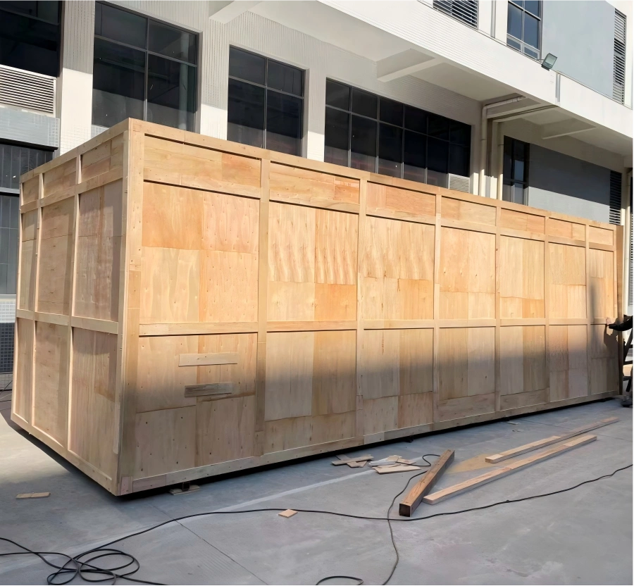 Extra large fully enclosed wooden case assembled on site outside factory with construction debris indicating recent on-site packing work