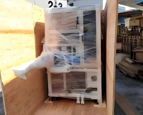 Industrial machine wrapped in stretch film positioned inside partially assembled wooden crate during on-site packing process