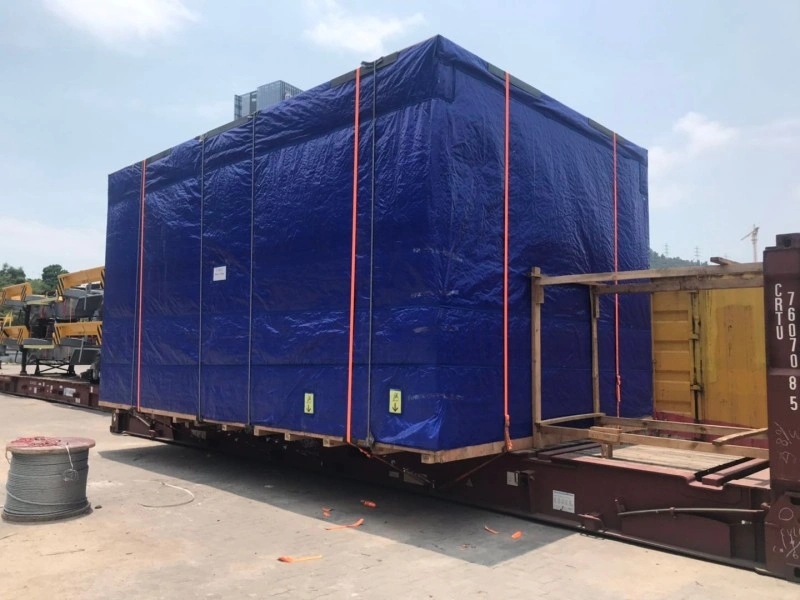 A close-up view of a blue-tarped, oversized industrial unit on a flat rack container, featuring red lashing straps and wooden bracing, showcasing optimized cargo securing for global transport.