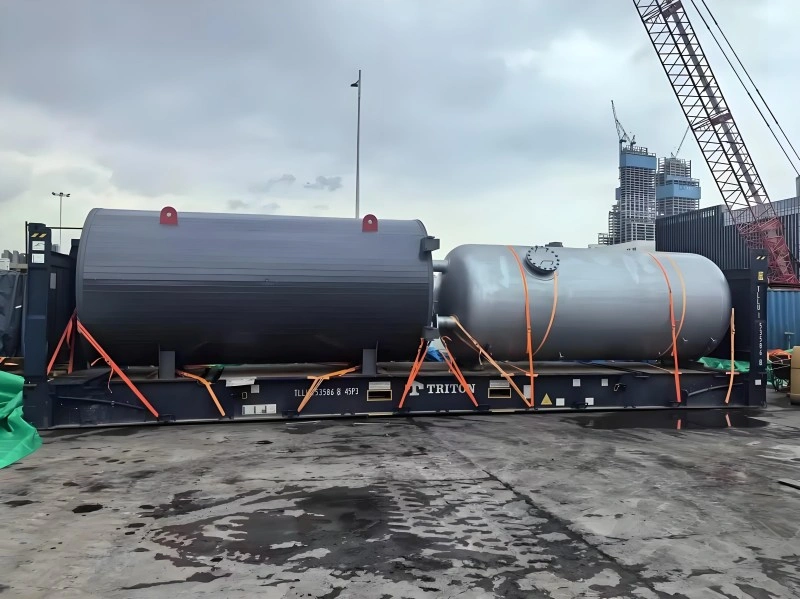Two oversized industrial pressure vessels secured with orange lashing straps on a Triton flat rack container, prepared for project cargo transport