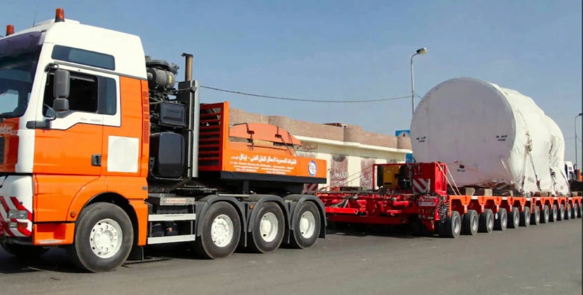 Oversized industrial machine transported on lowbed trailer convoy for factory delivery