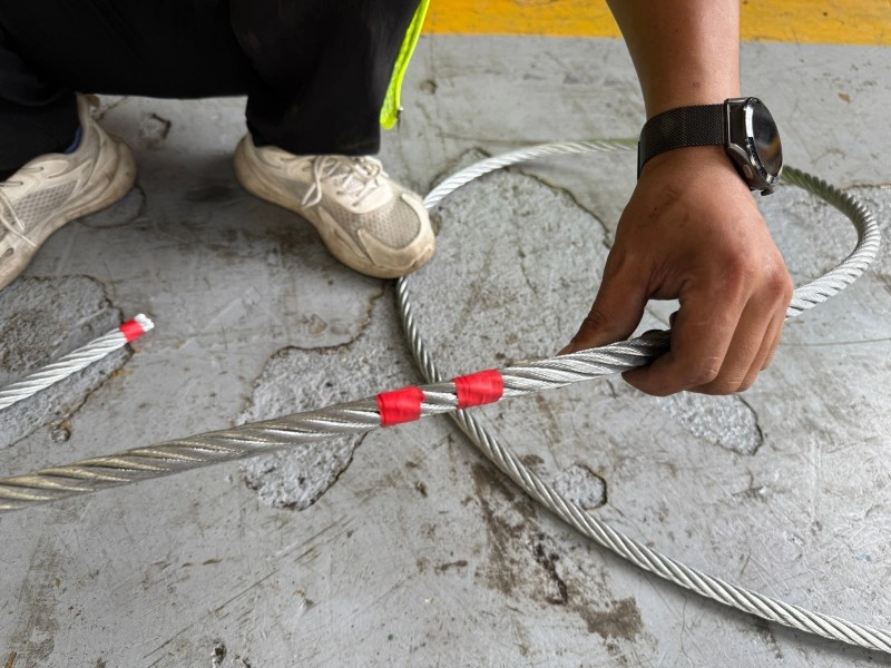 A logistics engineer inspecting a heavy-duty steel wire rope sling with red serving tape to ensure it is free of defects before lifting steel structures.