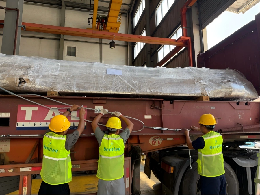 Bentlee logistics team securing shrink-wrapped cargo with turnbuckles and lashing rods on a TAL flatbed trailer before oversized shipment departure