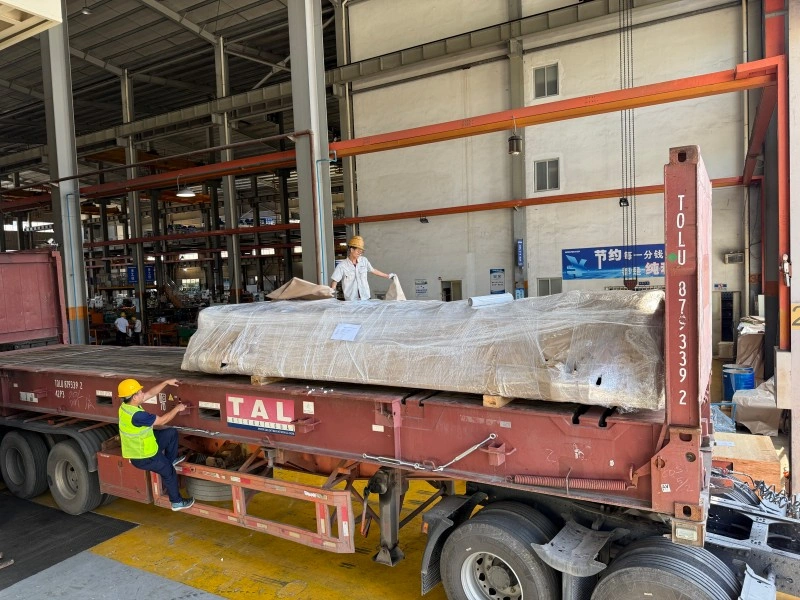 Logistics team loading export-packed industrial machinery onto a TAL flatbed trailer during pre-shipment preparation for factory relocation