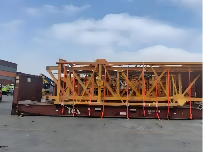 Yellow prefabricated steel truss frame mounted on brown flat rack and secured with orange lashing straps for modular construction project