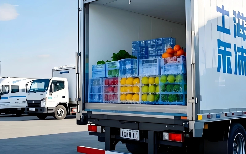 White refrigerated truck with open rear doors displaying blue crates of citrus fruits apples and leafy greens arranged for fresh produce cold chain delivery