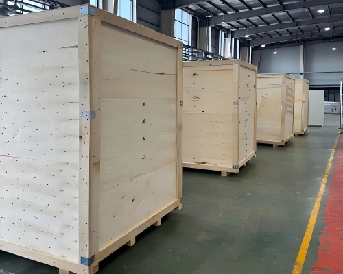 Custom built wooden crates with reinforced corners and metal fasteners lined up in factory warehouse for oversized equipment export packing