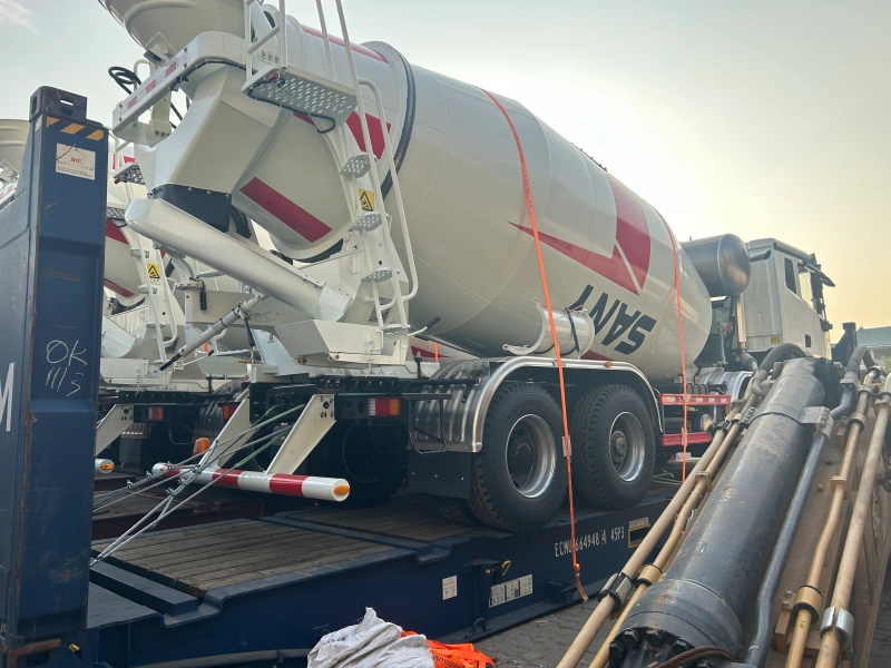 A white SANY concrete mixer truck with red stripes is securely strapped onto a blue flat rack container, prepared for oversized cargo shipping, with visible lashing belts and support structures ensuring stability.