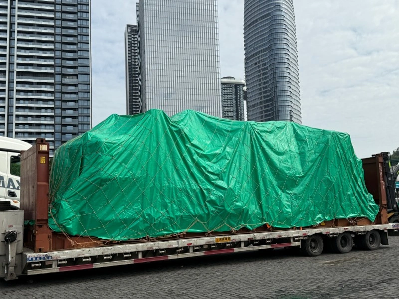 A fully covered OOG shipment secured with green tarp and cargo netting on a flatbed truck, ready for inland transportation with anti-theft measures in place.