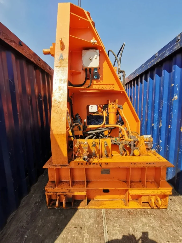 A close-up view of a heavy-duty orange machinery part, labeled "TOWER B IN BOARD," securely positioned inside a shipping container, showcasing the internal bracing and securement for safe transport.