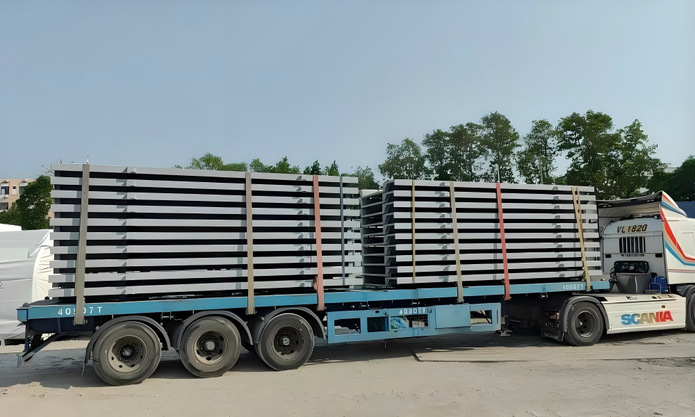 Two stacks of structural steel I beams loaded on blue flatbed trailer secured with wooden dunnage and red tension straps for construction site delivery