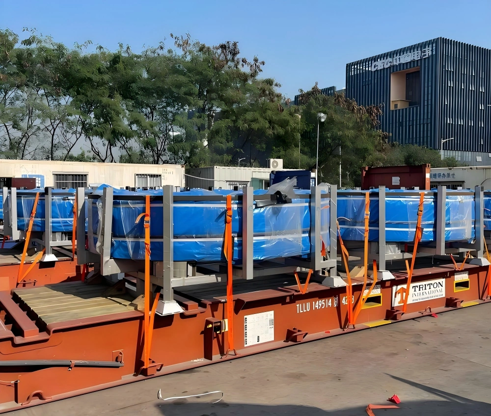 TRITON International flat rack trailer carrying multiple OOG cargo units covered in blue tarp and secured with orange lashing straps at logistics yard