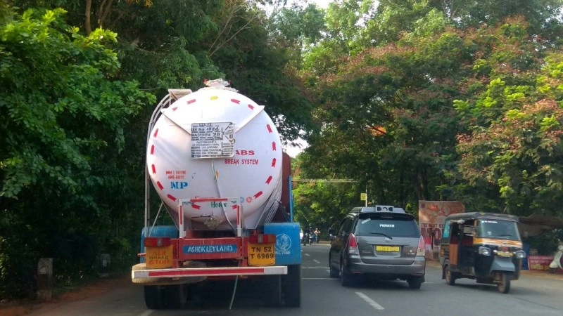 White tanker truck with hazard placards navigating a tree-lined road, illustrating real-world hazardous liquid transportation