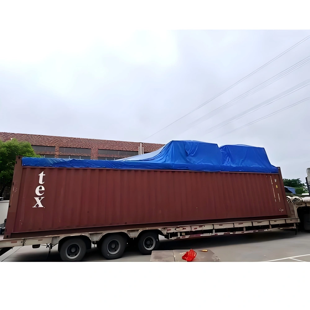 Over-height industrial cargo covered with blue tarpaulin on a red shipping container, prepared for open top transport with weather protection