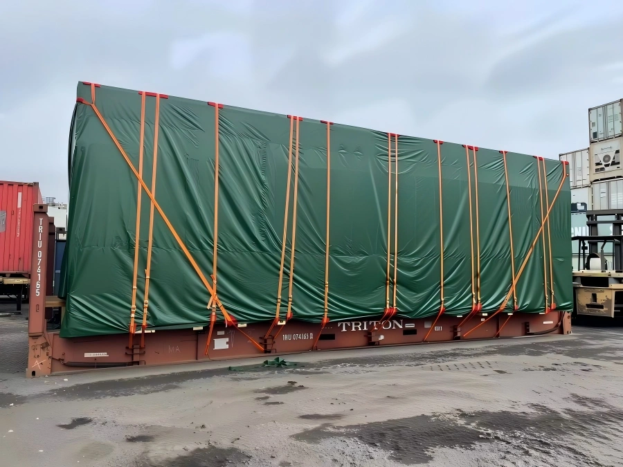 Oversized industrial cargo fully covered with green tarpaulin and secured by orange lashing straps on a TRITON flat rack container for OOG transport