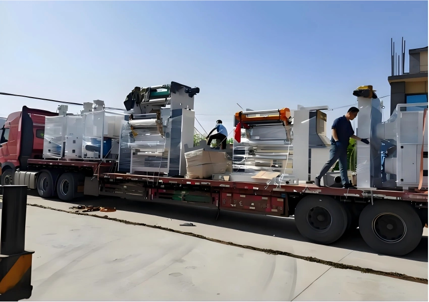 Workers securing vacuum packed industrial machinery including CNC machines and press components on red flat rack for manufacturing equipment relocation