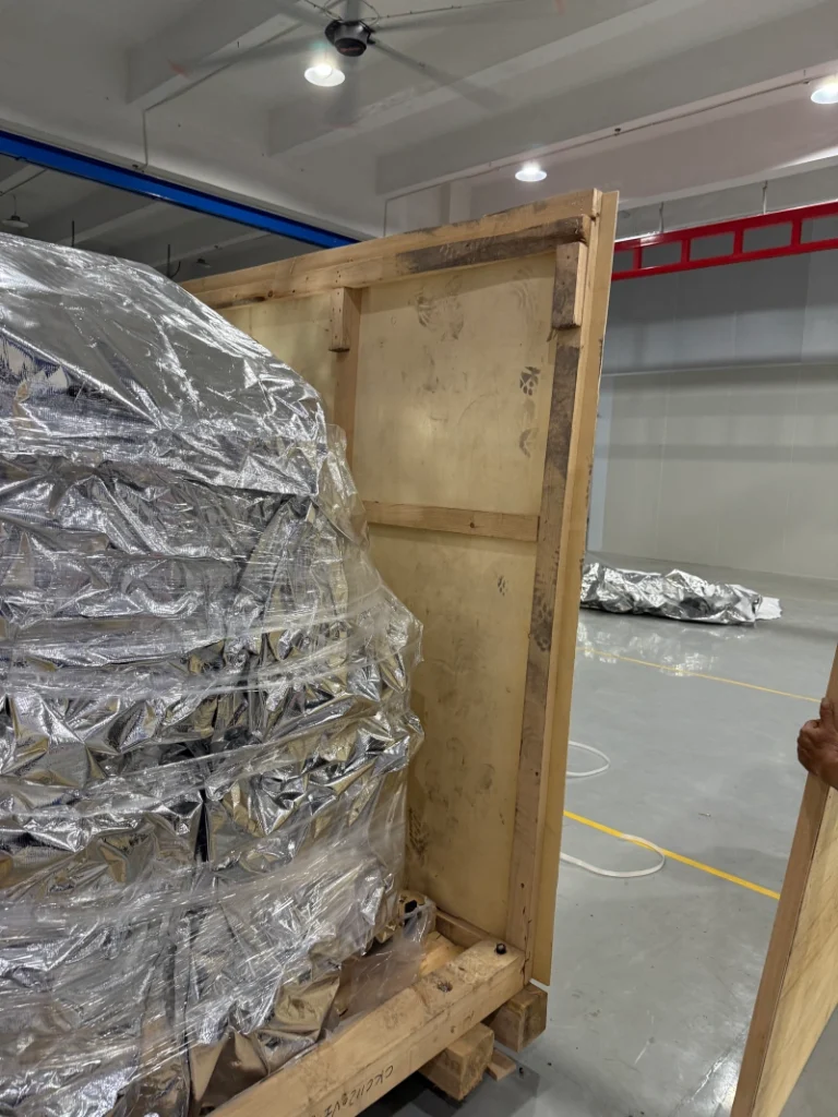 A close-up view of sensitive machinery components wrapped in silver aluminum foil barrier bags and secured on a wooden pallet base.