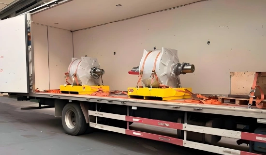 Two vacuum sealed industrial electric motors on yellow wooden skids loaded inside open trailer and secured with orange tension straps for mine equipment delivery
