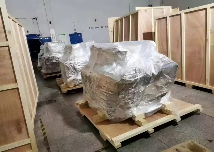 Two industrial machines on pallets vacuum sealed with clear film over silver moisture barrier inside warehouse ready for container loading