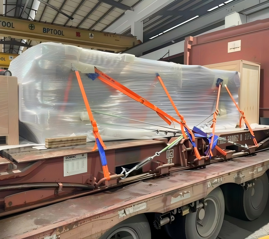 Vacuum sealed modular unit on red flat rack secured with multi color tension straps under factory overhead crane for site office transport