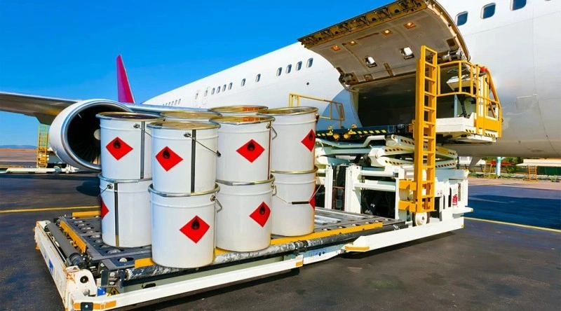 White metal drums with red flammable liquid hazard labels being loaded onto a cargo aircraft via a hydraulic lift platform