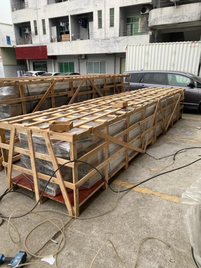 Multiple identical wooden crates lined up outdoors near shipping container, showcasing standardized manufacturing and readiness for bulk international freight