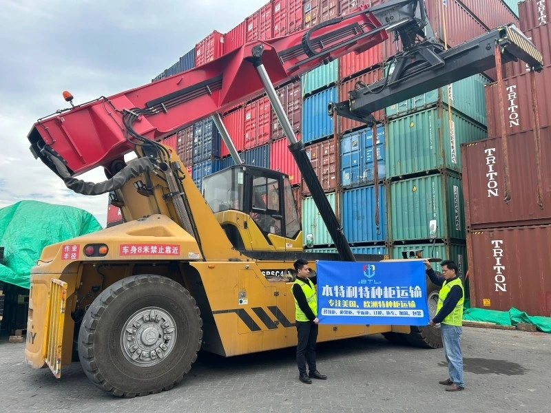 Yellow reach stacker lifting a container at a busy port terminal, illustrating synchronized multimodal equipment transfer for oversized cargo.