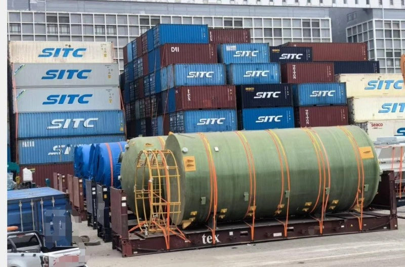 Two massive green industrial tanks loaded on flat racks, positioned among stacks of SITC containers, highlighting the scale and coordination required in production line relocation logistics.