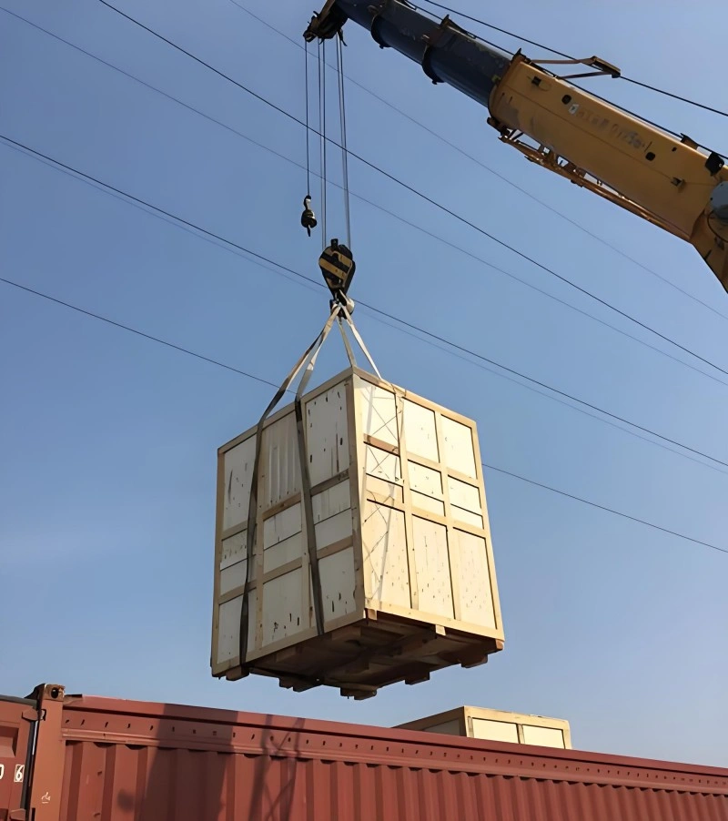A mobile crane hoisting a large, reinforced wooden crate onto a shipping container, showcasing professional handling and structural integrity for oversized cargo logistics.