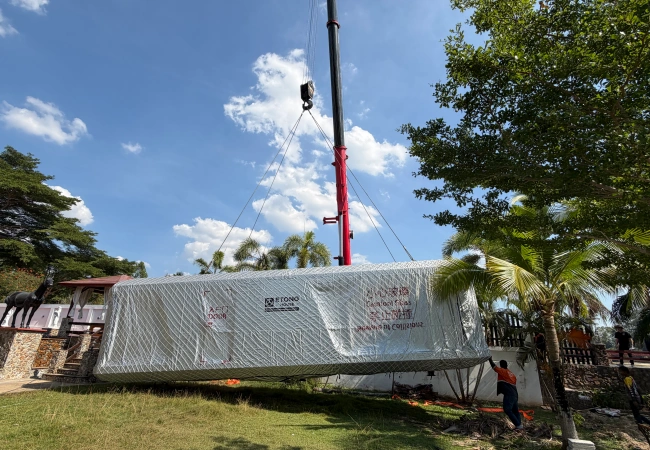 A crane lifting a wrapped space capsule cabin in an outdoor setting, demonstrating the final stage of delivery for a glamping resort project