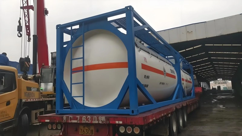 A large red and yellow mobile crane is lifting a blue-framed ISO tank container, which holds two white cylindrical tanks with orange hazard stripes. The container is being positioned onto a red multi-axle flatbed trailer in an industrial yard with buildings in the background.
