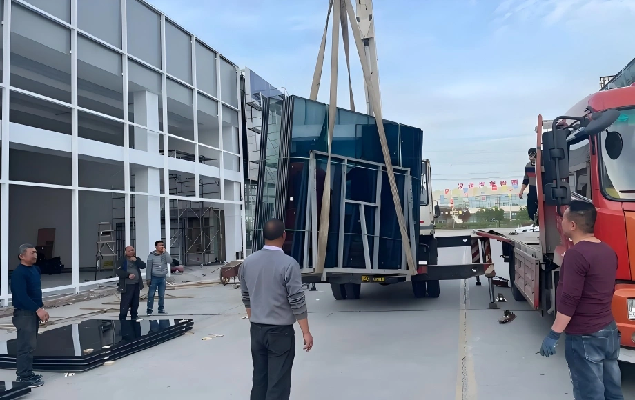 Logistics team using a crane to safely lift a rack of glass curtain wall units onto a truck, demonstrating careful handling for fragile OOG cargo.