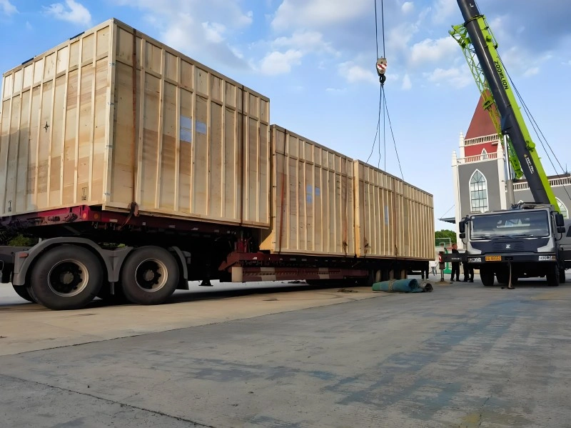 A mobile crane lifting oversized wooden crates onto a heavy-duty flatbed trailer, demonstrating professional handling and secure logistics for industrial machinery export packaging.