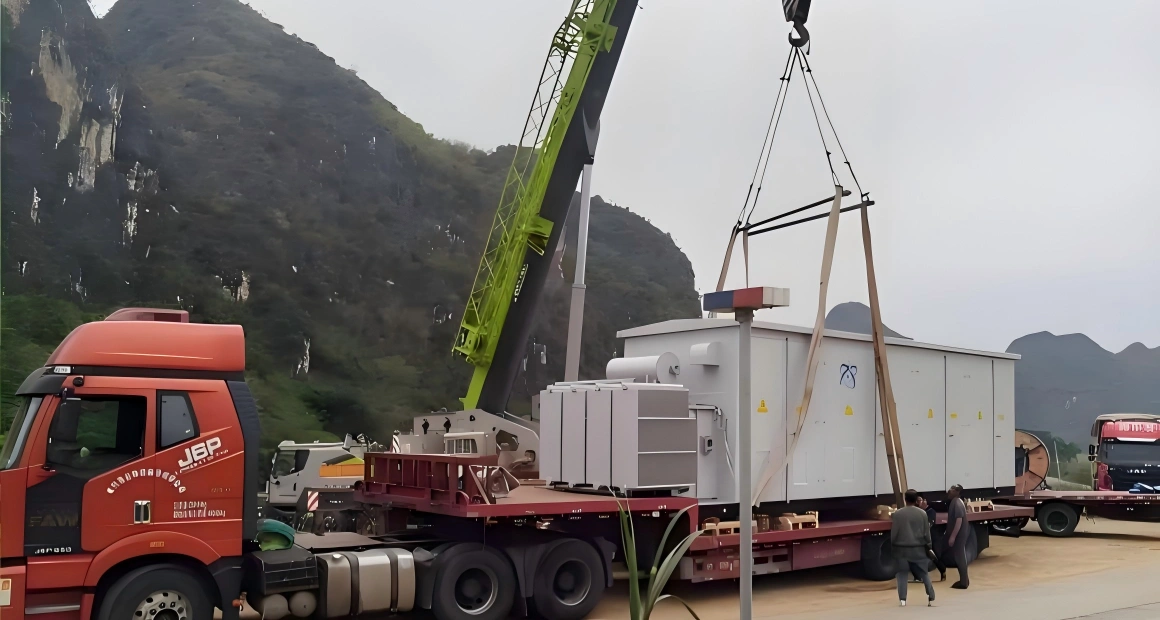 Heavy-duty crane lifting a large white transformer unit onto a flatbed truck, highlighting precise loading operations for sensitive power equipment