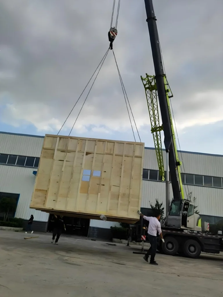 A mobile crane lifting a large, reinforced wooden export crate onto a truck bed, showcasing professional handling and structural integrity for oversized cargo logistics.