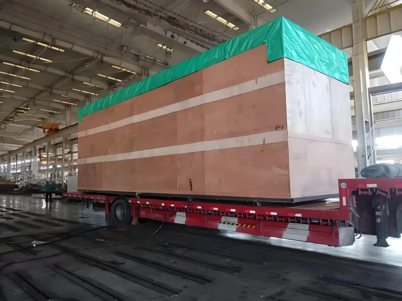 Worker sealing a large metal equipment with silver aluminum vacuum packaging material outdoors, ensuring waterproof and anti-corrosion protection.