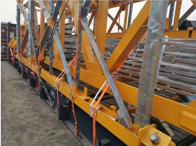 Close-up shot showing orange ratchet straps, chains, and protective padding used to secure a yellow metal frame to a flat rack, highlighting best practices in cargo stabilization.