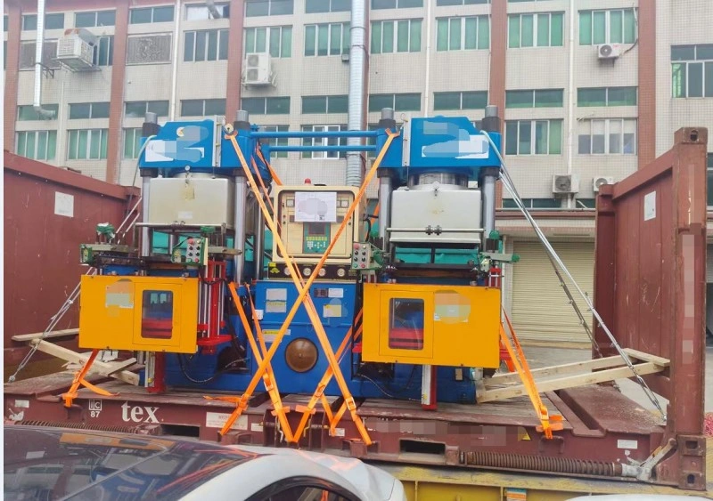 Two blue-and-yellow hydraulic press machines mounted side-by-side on a red flat rack container, secured with diagonal orange straps forming X-patterns; wooden blocking and metal brackets visible beneath units; urban factory buildings in background.
