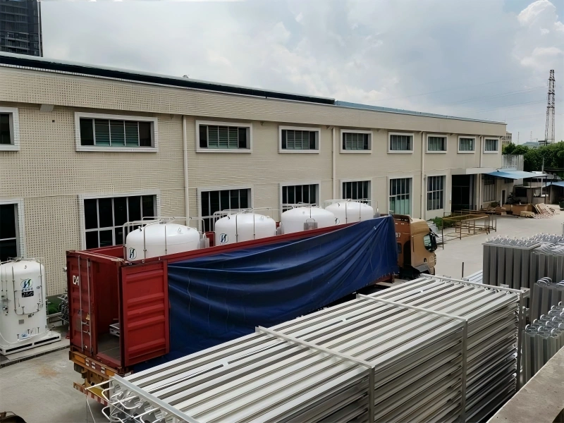 Multiple white industrial tanks loaded onto a truck with blue tarp cover, parked outside a factory building, ready for shipment to port.