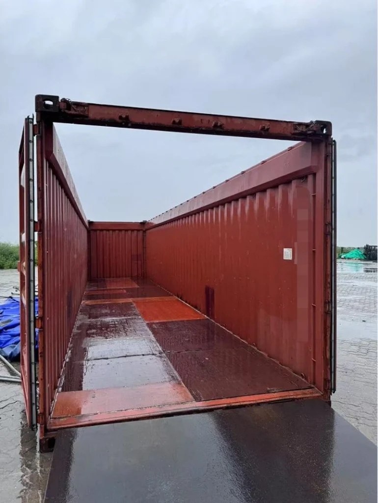 The interior of an empty open top container reveals a reinforced wooden floor with metal edging, designed to support heavy loads and withstand the stress of crane lifting operations.